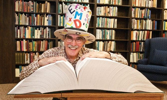 Man with crazy letter tophat smiling reading a book